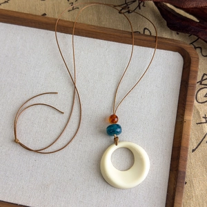 Détail du collier rétro chinois avec anneau crème et perles d'ambre sur cordon