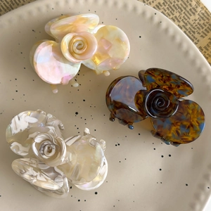 Three acetate rose flower hair claws in tortoiseshell and marble patterns on ceramic plate