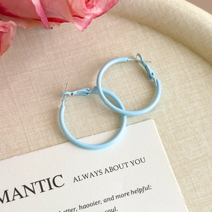 Detail of light blue matte hoop earrings on white fabric with rose and card decoration