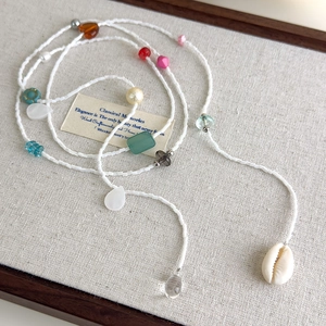 Collier de perles colorées avec pendentif coquillage naturel sur fond de lin rustique