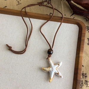 Détail du pendentif étoile de mer en céramique sur cordon brun avec perle en bois