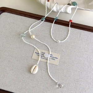 Collier bohème en perles avec pendentif coquillage et accents colorés sur lin