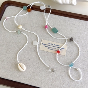 Détail d'une chaîne longue bohème en perles colorées avec pendentif coquillage sur lin