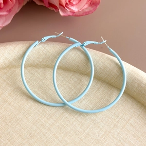 Detail of large baby blue hoop earrings with matte finish on a beige textured tray