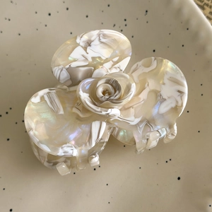 Detail view of cream acetate camellia hair claw with marble texture on ceramic plate