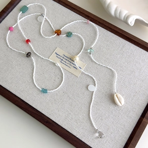 Détail d'un collier bohème avec perles de coquillage colorées sur un plateau en lin