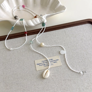 Détail d'un collier bohème avec perles colorées et pendentifs coquillages sur plateau
