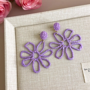 Detailed macro view of purple raffia woven flower earrings on a beige display tray