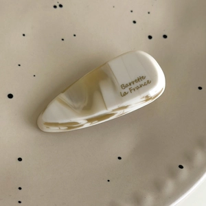 Détail d'une barrette goutte en acétate marbré crème sur un plat en céramique
