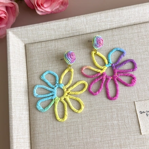 Detailed close-up of handmade raffia flower earrings on a textured jewelry display tray