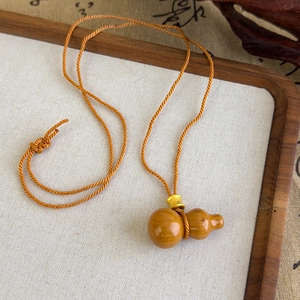Détail d'un pendentif en bois en forme de gourde avec cordon orange et perle dorée