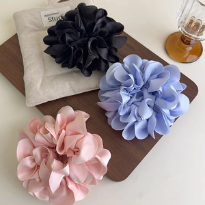 Trois chouchous fleurs en satin rose, bleu et noir posés sur un plateau en bois