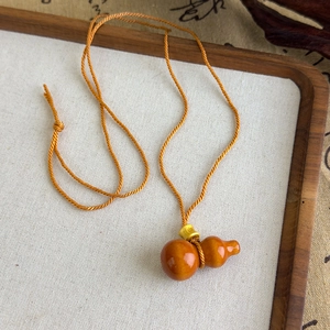 Détail du pendentif gourde ambrée avec perle dorée sur cordon ethnique tressé