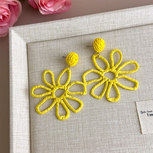Detail of yellow woven straw flower earrings on a display tray with floral accents