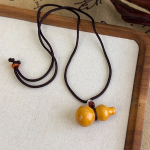 Gros plan d'un pendentif gourde en bois fait main avec corde tressée sur plateau en lin