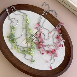 Pink and green layered beaded floral choker necklace on a wooden jewelry display tray