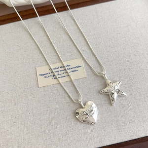 Detailed view of hammered silver necklaces with heart and star charms on linen