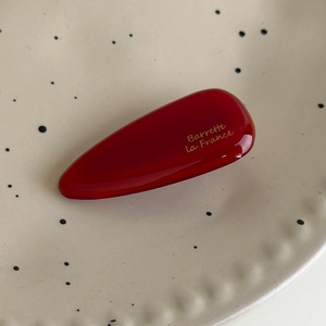 Détail d'une barrette goutte en résine rouge foncé avec lettrage doré sur un plateau