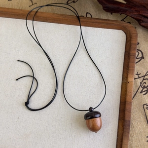 Gros plan détaillé d'un pendentif gland en bois fait main sur un collier de corde noire