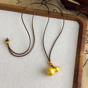 Détail du pendentif calebasse dorée avec finition mate sur cordon tressé marron