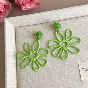 Detailed close-up of handmade green woven straw flower earrings on a textured fabric