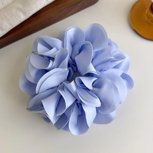 Gros plan d'un chouchou en satin bleu clair avec des plis en pétales sur fond épuré