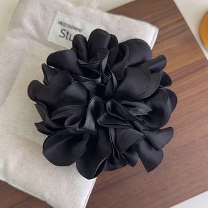 Gros plan d'un grand chouchou fleur en satin noir avec textures de pétales superposés