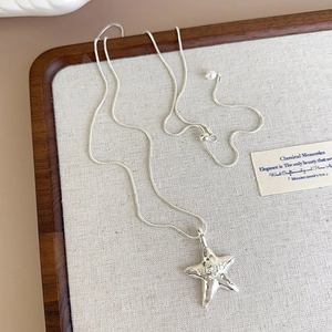 Macro detail of star pendant with letter engraving and silver snake chain with pearl