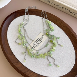 Detail of layered silver chain necklace with light green floral beads on a wooden tray