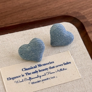 Macro detail of blue polka dot denim heart stud earrings on a vintage wooden tray