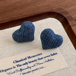 Macro detail of heart-shaped denim fabric earrings on a rustic display tray