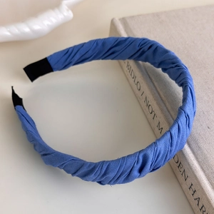 Detail of blue pleated fabric headband with protective black tips on a white book