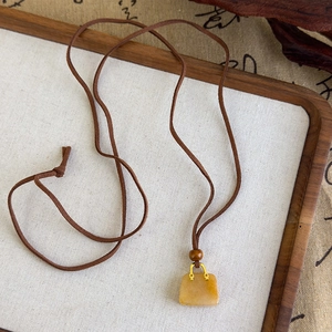 Vue détaillée d'un pendentif sac en pierre jaune avec poignée dorée et cordon marron