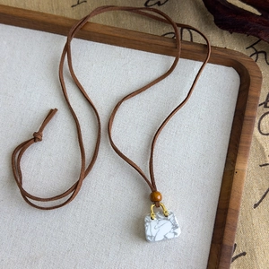 Détail du pendentif en pierre en forme de sac avec cordon en daim et perle en bois
