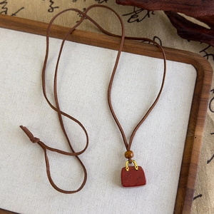 Détail d'un pendentif sac à main en agate rouge avec boucle dorée sur cordon marron