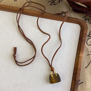 Vue macro d'un pendentif mini sac en oeil de tigre avec collier cordon tressé