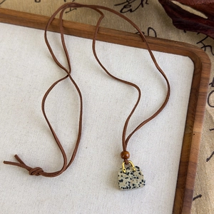 Détail du pendentif en pierre tachetée avec cordon marron et perles en bois style zen