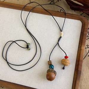 Gros plan d'un long collier ethnique avec pendentif gland en bois et perles céramiques
