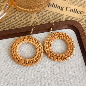 Detail von handgefertigten runden Strohohrringen mit Goldhaken auf Vintage-Hintergrund