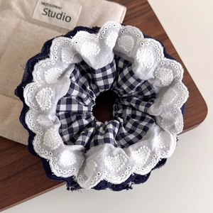 Close-up of navy plaid fabric scrunchie featuring delicate white heart embroidery lace edge