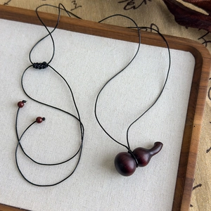 Détail du pendentif calebasse en bois artisanal sur un collier de cordon tressé noir