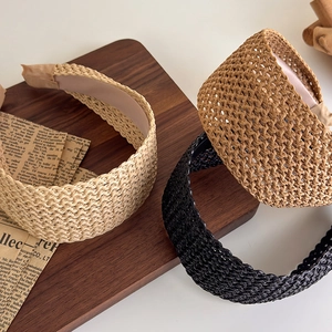 Trois serre-têtes en paille tressée beige marron et noir sur plateau en bois