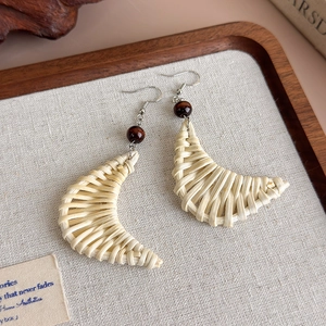 Close-up detail of moon-shaped woven wood fiber drop earrings with red bead accent
