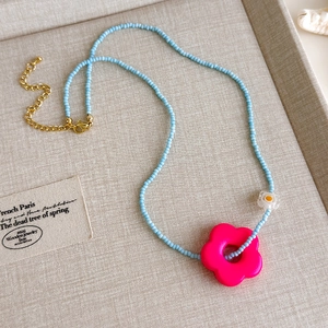 Nahaufnahme einer blauen Perlenkette mit rosa Blumenanhänger und goldener Verlängerung