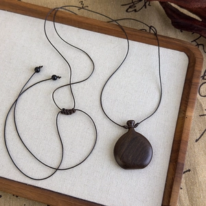 Vue macro d'un pendentif en bois poli sur un collier en corde tressée réglable marron