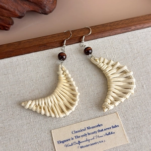 Close-up of crescent-shaped woven straw earrings with a dark brown wooden bead accent