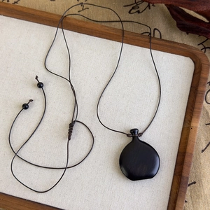 Détail du collier en corde tressée main avec pendentif en ébène poli sur fond style zen