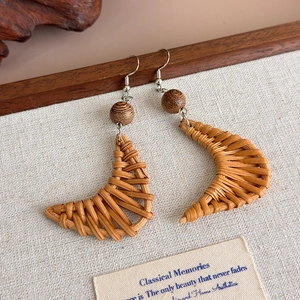 Detail of handmade woven crescent earrings with dark brown wood beads and silver hooks