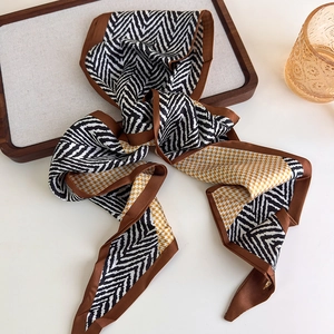 Close-up of a long silk twilly scarf with houndstooth and wavy patterns on a tray