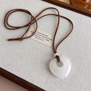 Detailed macro view of heart-shaped white stone pendant on brown suede cord necklace